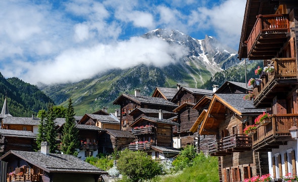 A wooden chalet in a picturesque Swiss village, with green mountains in the background.